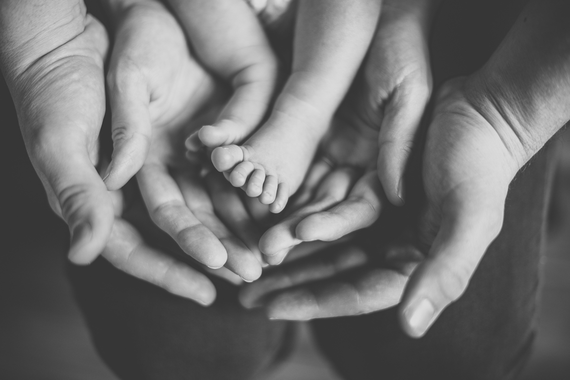 Newborn photo-shoot - newborn's feet surrounded by the hands of his parents - Newborn Photographer