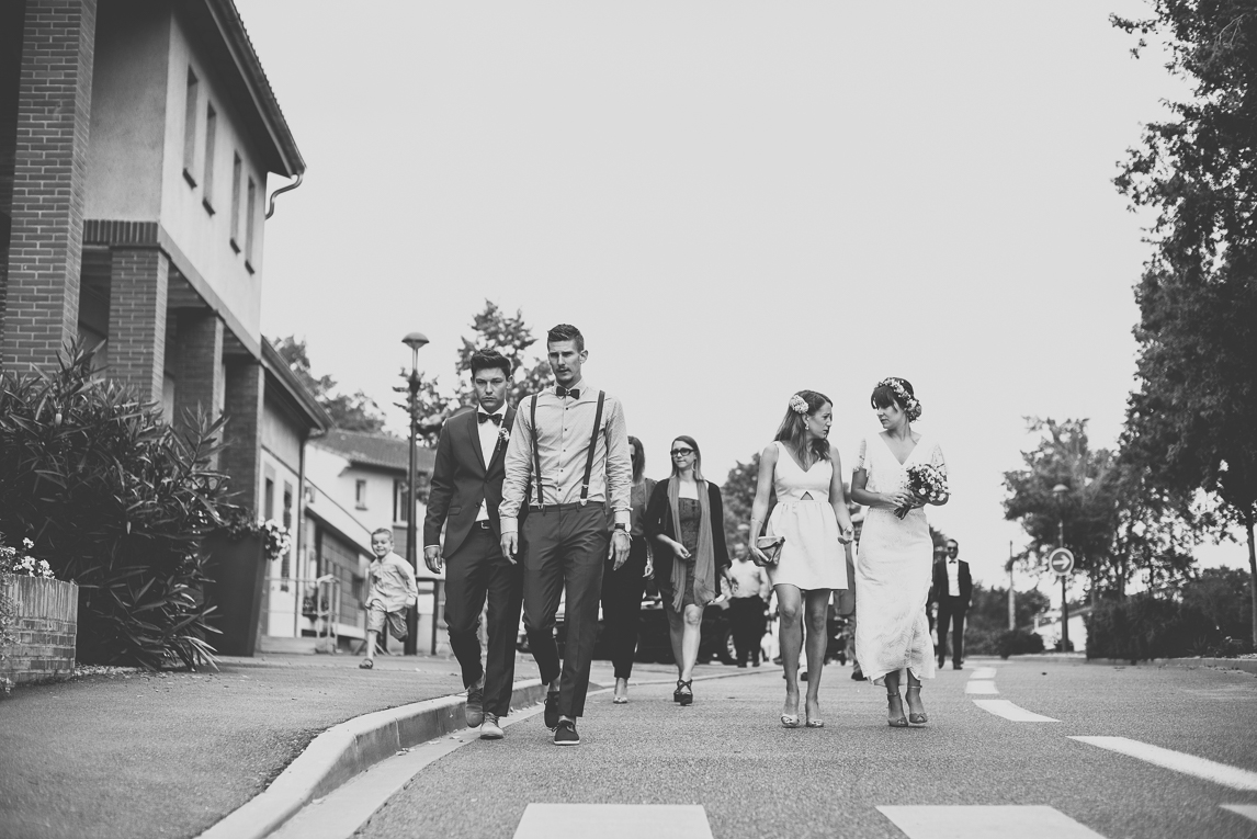 Reportage mariage Toulouse - mariés et invités marchent sur la route - Photographe mariage