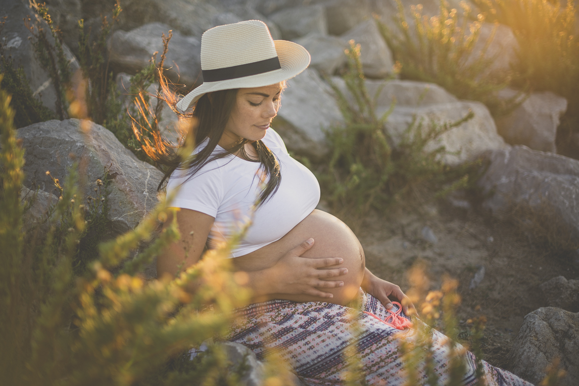 Séance photo grossesse à la plage - femme enceinte assise parmis les rochers au coucher du soleil - Photographe grossesse