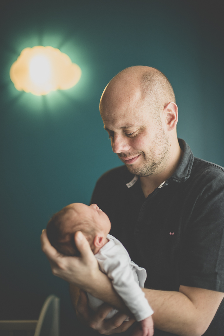 Séance photo nouveau-né Muret - papa tient bébé dans ses bras et le regarde - Photographe naissance