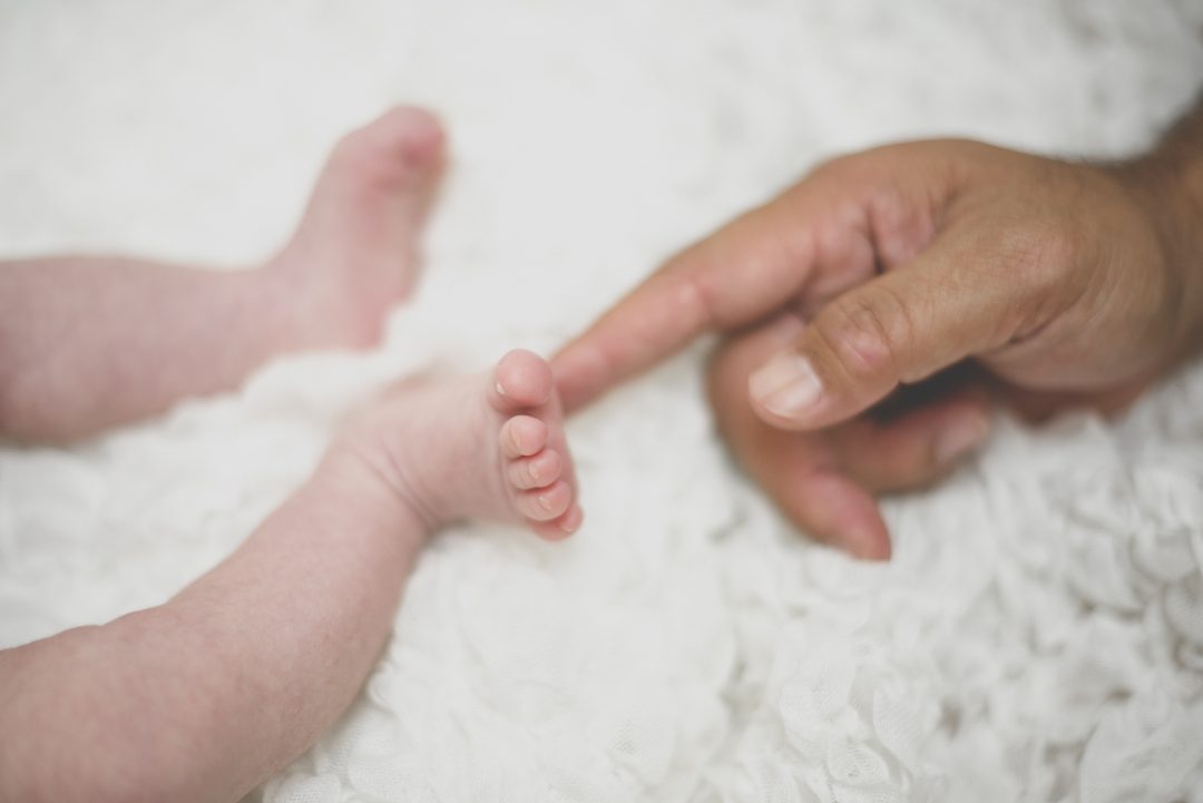 Séance photo naissance à domicile Occitanie - main de papa touche pied du nouveau-né - Photographe naissance