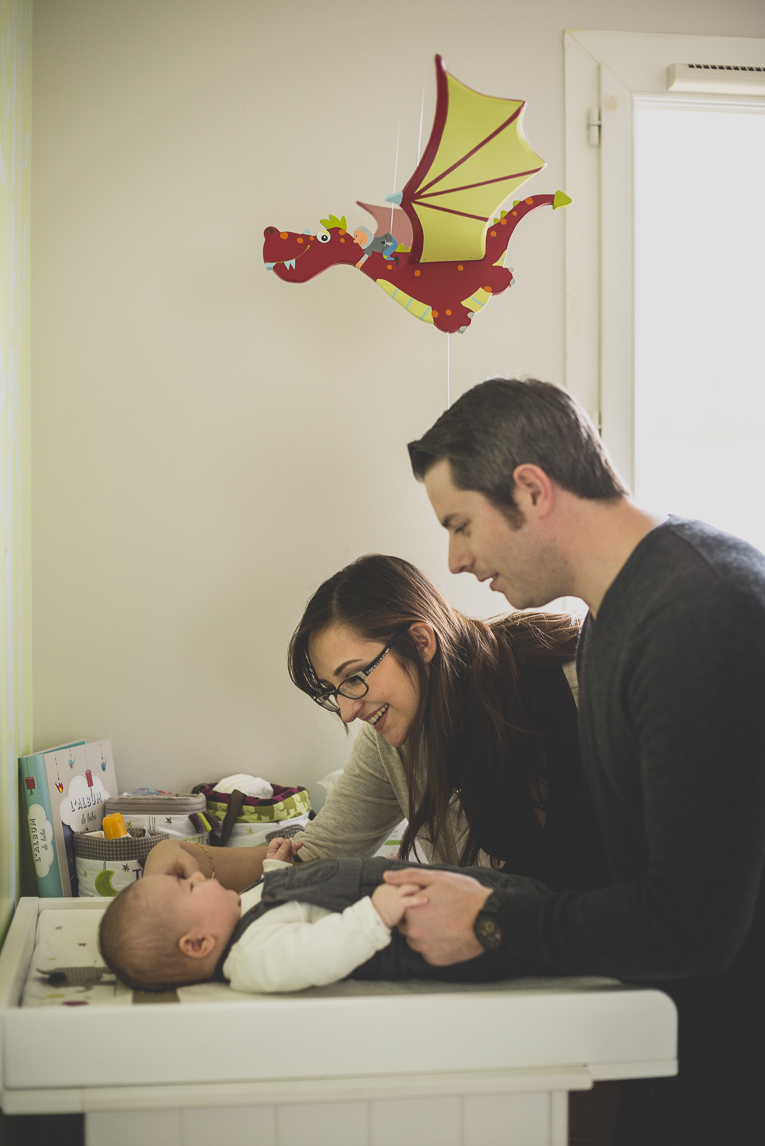 Séance bébé à domicile - parents regardent leur bébé sur table à langer - Photographe bébé