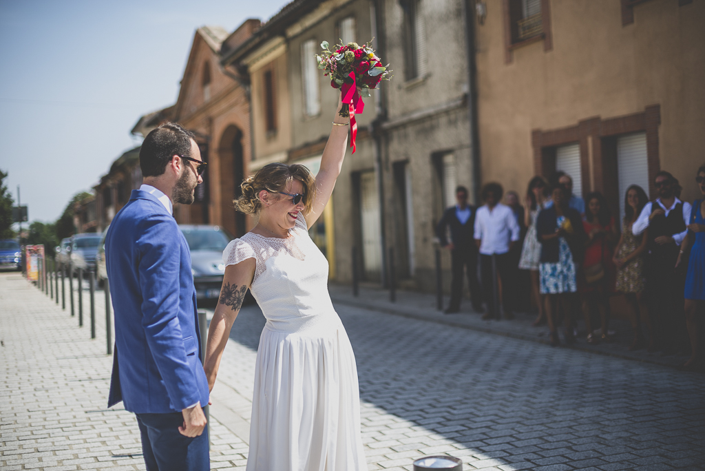 Reportage mariage Haute-Garonne - mariée lève son bouquet devant invités - Photographe mariage